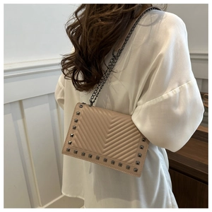 Detail of nude quilted crossbody bag featuring silver studs and dark grey metal chain strap