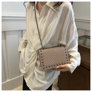 Detail view of beige crossbody bag with metal chain strap and rivet trim on white shirt