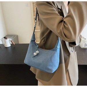 Détail du sac croissant en denim bleu clair avec matelassage et breloque en perles