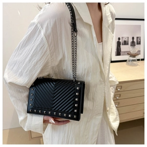Detail of black crossbody bag featuring silver studs and V-shaped quilted texture on the flap
