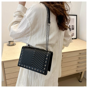 Black V-quilted shoulder bag with silver studs and chain strap worn by a model