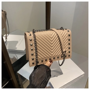 Macro detail of beige quilted leather bag with V-shaped stitching and dark metal rivets