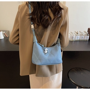 Détail du sac cylindre en denim bleu clair avec coutures matelassées et perle décor