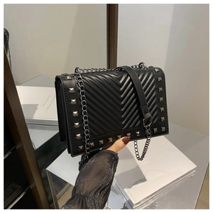 Detail of black quilted shoulder bag featuring silver rivets and metal chain strap