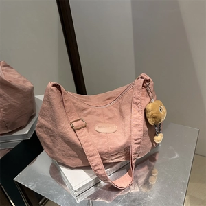 Pink crescent nylon tote bag with adjustable strap and cute plush charm on silver display