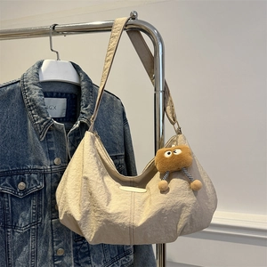 Beige crescent hobo bag with pleated texture and plush charm on a metal display