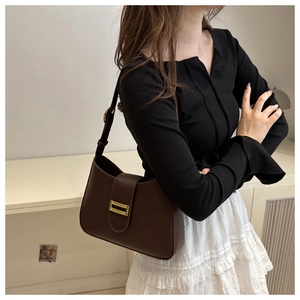 Detail of dark brown leather shoulder bag with a vintage gold buckle on a female model