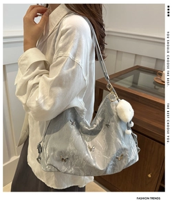 Close-up of silver-grey textured shoulder bag with metal butterfly charms and plush ball