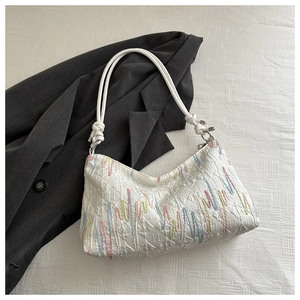Detailed close-up of white quilted tote bag with colorful vertical embroidery and rope knot