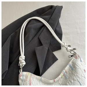 Detail of white textured shoulder bag featuring colorful embroidery and knotted strap