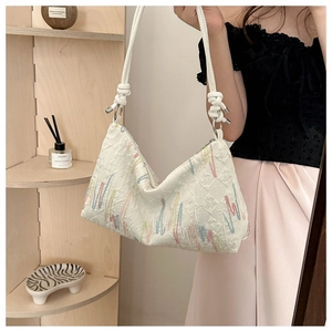 Close-up of white crossbody bag with wave embroidery and knotted rope strap detail