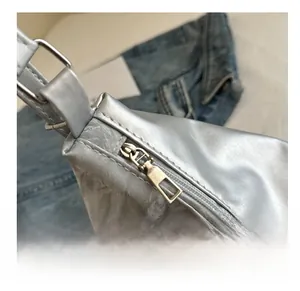 Detailed macro view of a silver metallic crossbody bag with smooth zipper and butterfly charm