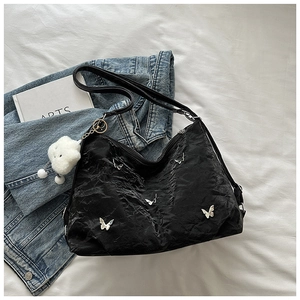 Detailed close-up of a black pleated tote bag with silver butterfly charms and plush charm
