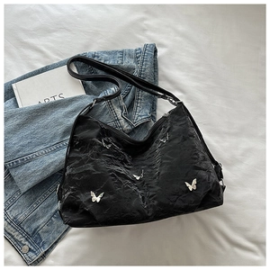Close-up of black pleated underarm bag with silver metal butterfly accents on a blue jacket
