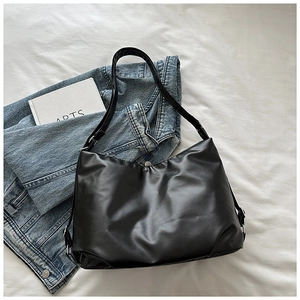 Flat lay of black leather tote bag with silver buckles on white textured linen sheet