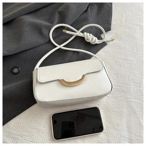 Detail der weißen Baguette-Tasche mit goldener Schnalle und Seilträger neben Smartphone