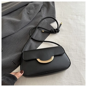 Minimalistische schwarze Baguette-Tasche mit goldener Mondschnalle auf grauem Blazer