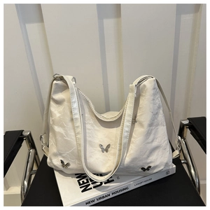 Detail of white pleated tote bag featuring silver butterfly metal accents on textured fabric