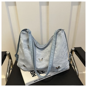 Detail of light blue pleated shoulder bag with silver butterfly studs on a black seat