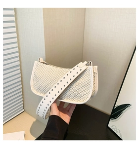 Detail of white woven straw bag featuring wide shoulder strap with silver rivet accents