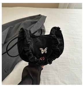 Detail of black satin crescent bag featuring pleated edges and silver butterfly buckle