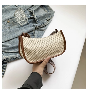 Detail of hand-woven straw shoulder bag featuring brown leather trim and metal rivets