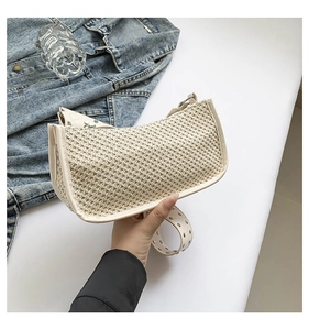 Detail of straw woven crescent bag with leather trim and silver metal rivet shoulder strap
