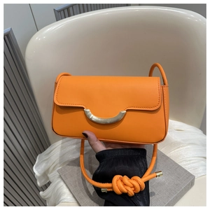 Detail of bright orange leather flap bag featuring a golden half-moon clasp and rope knot strap