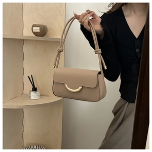 Detailansicht der beigen Baguette-Tasche mit goldenem Verschluss und geknotetem Riemen