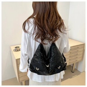 Detail of black pleated backpack with silver butterfly accents shown on model's back