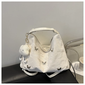 White ruched tote bag with silver butterfly charms and cloud pendant on a leather bench