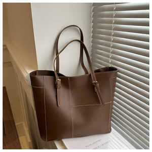 Detail view of large brown tote bag featuring white contrast stitching and matte leather texture