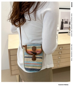Detailed view of rainbow straw crossbody phone bag with wooden toggle and leather trim