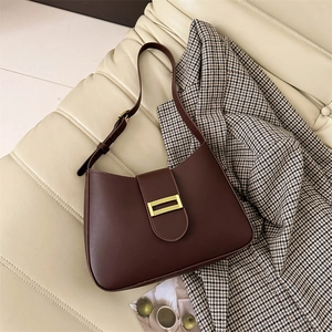 Minimalist dark brown leather baguette underarm bag with gold buckle on a cream sofa