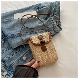 Close-up of woven straw phone bag with brown faux leather trim and horn buckle detail