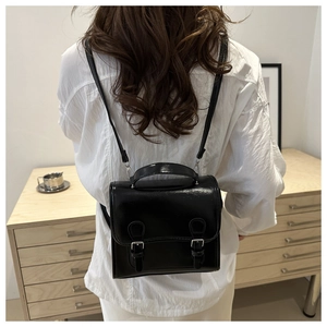 Back view of a glossy black leather mini backpack worn by a model in a minimalist room