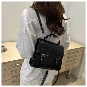 Close-up of black glossy leather backpack featuring vintage double buckle flap and top handle