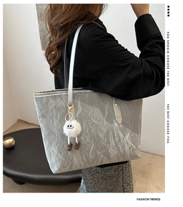 Detail of silver crinkled tote bag featuring a cute white plush monster charm on shoulder