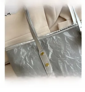 Detail of silver pleated tote bag featuring gold metallic rivets and minimalist strap design