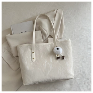 Detailed close-up of white tote bag with pleated texture and a cute monster pendant