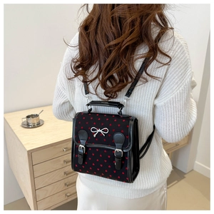Detail of black backpack with red heart patterns and silver bow on textured surface