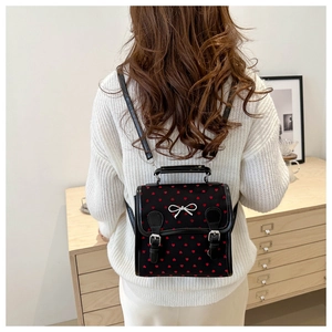 Close-up of a black mini backpack with red hearts and a silver bow detail worn by a model