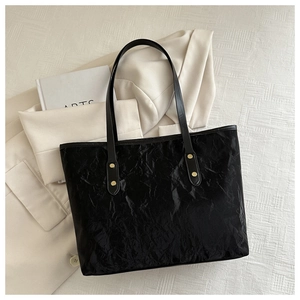 Detail of black tote bag with wrinkled texture, leather handles and gold rivet accents