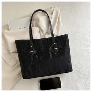 Close-up of black tote bag with wrinkled texture, leather straps and gold metal rivets