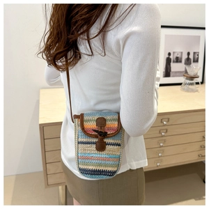 Detail of colorful woven phone bag featuring a brown leather flap and black toggle button