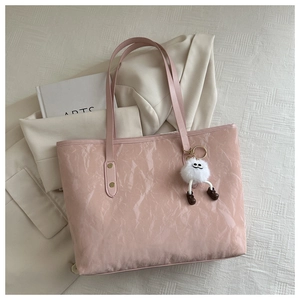 Detail of pink glossy tote bag with plush charm on a beige blazer background
