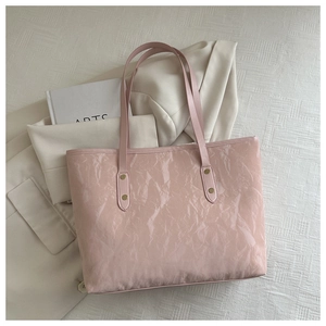 Detailed close-up of pink tote bag with glossy pleated texture and gold rivet hardware