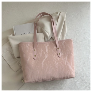 Detail of pink tote bag showing glossy wrinkled leather texture and golden rivets