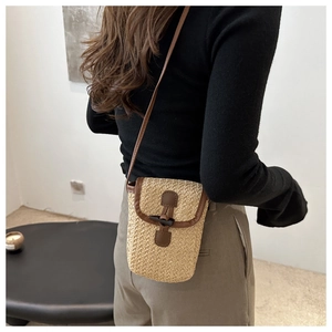 Detailed view of hand-woven straw crossbody bag with brown leather strap and horn button