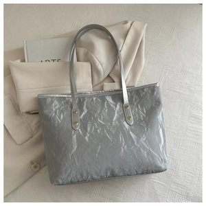Close-up of a silver tote bag with pleated texture, gold rivets, and a gray shoulder strap